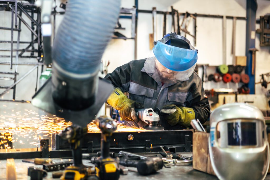 Mitarbeiter in Schutzkleidung schleift ein Werkstück, Funken sprühen