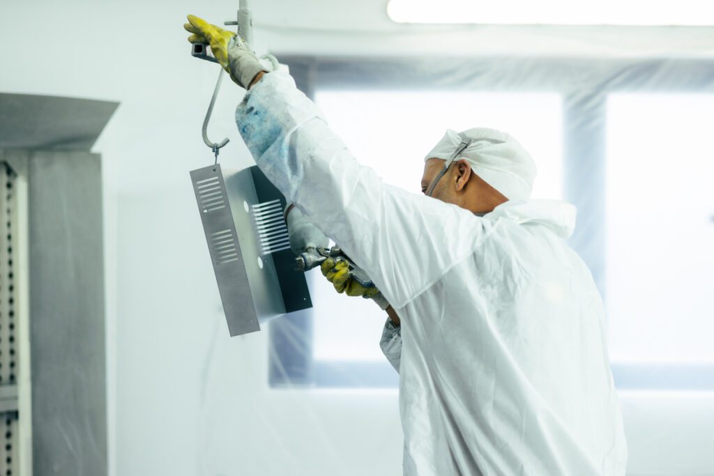 Mitarbeiter sprüht ein Werkteil mit weißer Farbe ein